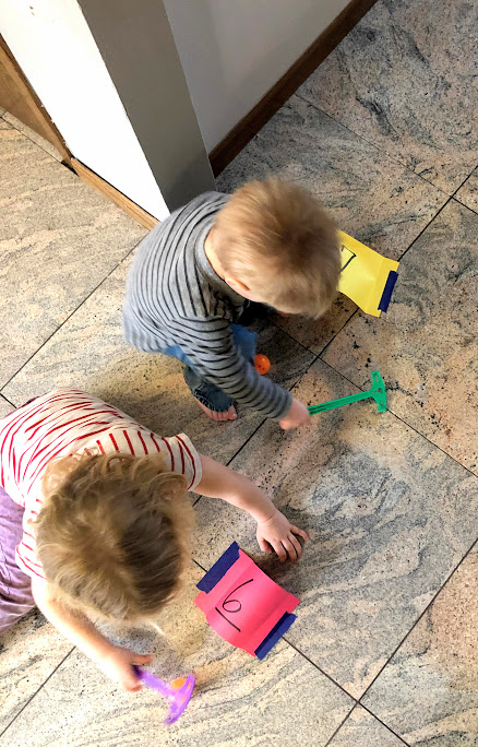 Two young kids playing indoor croquet for movement activities for preschoolers and their parents.