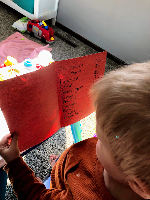 Boy reading a homemade menu for  simple dramatic play ideas for young kids