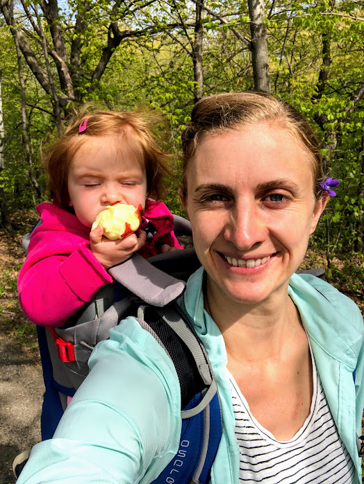 toddler eating an apple in a hiking backpack on woman's back