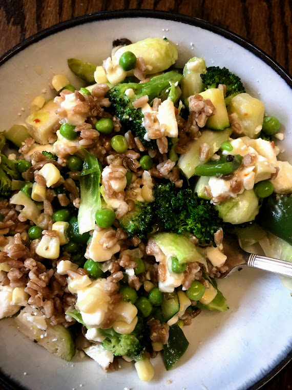 Farro toss with broccoli, lettuce, peas, feta, brussels sprouts in a bowl